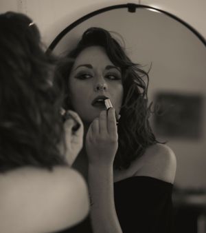 Black and white photo of applying lipstick in front of mirror showing vintage glamour and beauty.