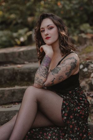 Artistic portrait of alternative model in floral dress and fishnet stockings sitting on stone steps.