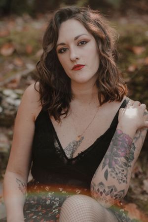 Alternative style portrait with visible tattoo artwork wearing black lace top in autumn setting.