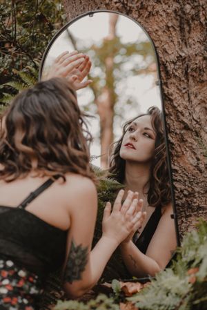 Ethereal outdoor portrait with vintage mirror reflection among trees and natural elements.