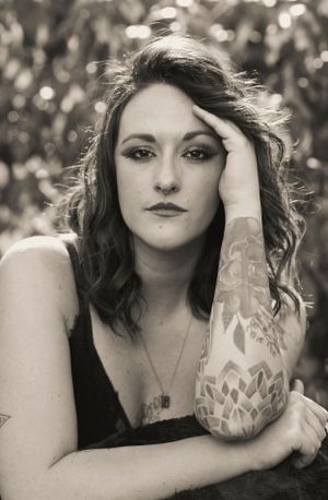 Monochrome portrait showing artistic pose with detailed arm tattoo sleeve.