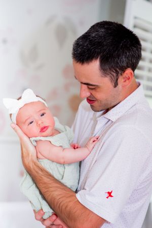 An infant in mint green outfit and white bow headband rests in gentle arms.