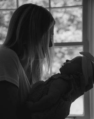 A silhouetted figure holds a baby near a window in this intimate black and white photograph.