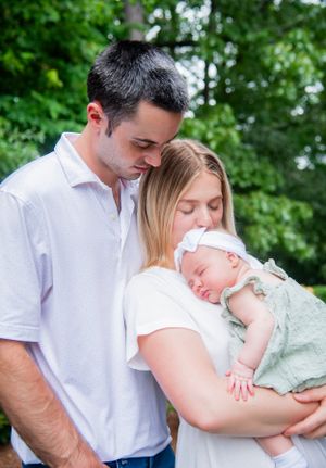 A tender outdoor family moment as parents embrace their sleeping newborn baby.