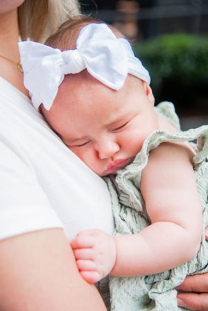 A sleeping baby with white bow headband nestles against a shoulder in a peaceful portrait.