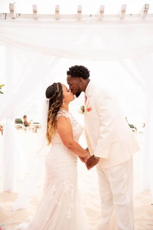 A couple shares their first kiss as newlyweds under a white wedding arch on the beach.
