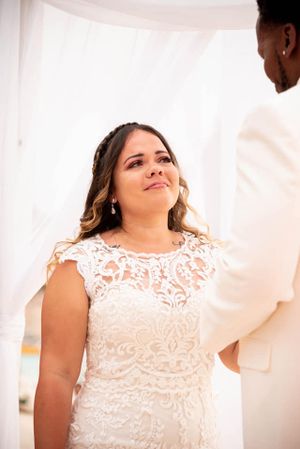 A bride in an elegant lace wedding dress smiles during her beach ceremony.