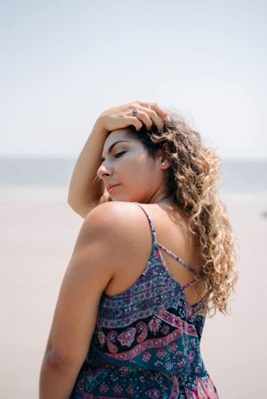 Woman in floral sundress with curly hair poses against a bright sky at golden hour.
