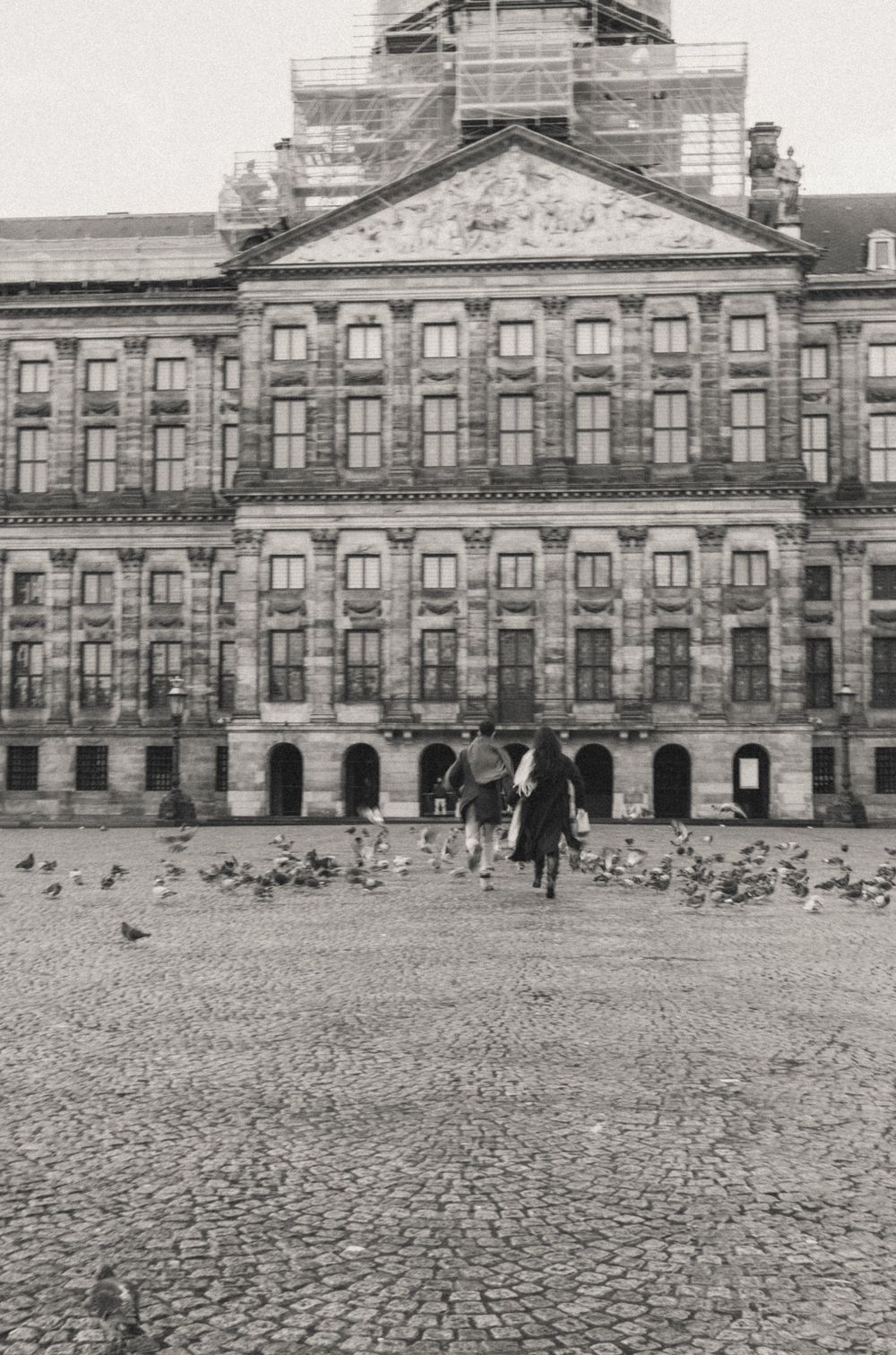 Historic stone building facade with cobblestone plaza and pigeons in black and white photography.
