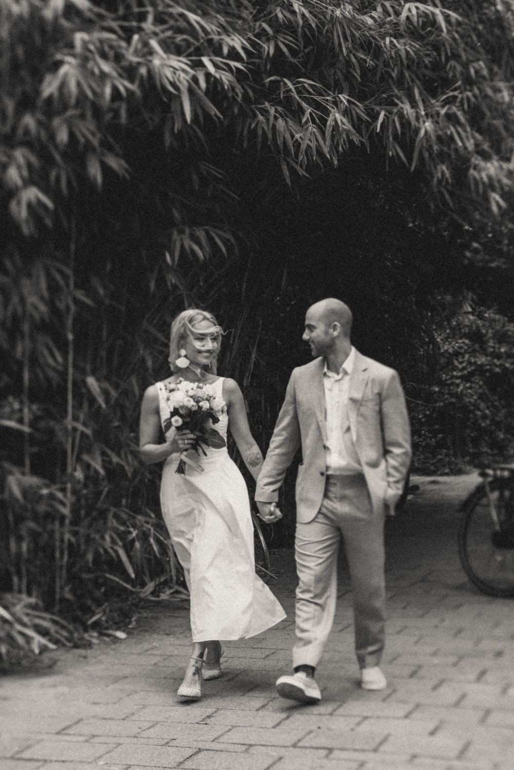 A couple strolls together on a garden path surrounded by bamboo plants.