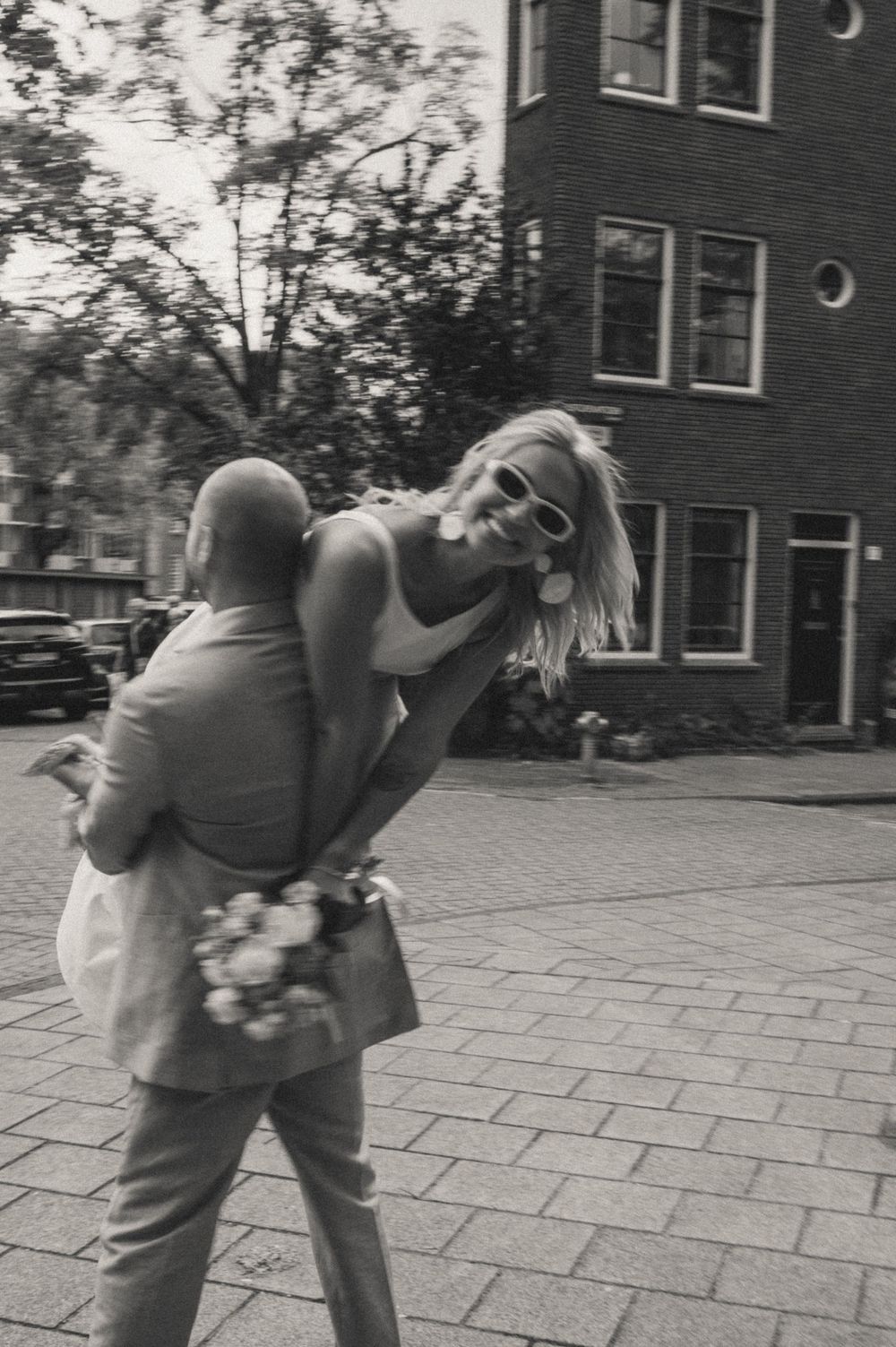 A couple dances playfully on a cobblestone street in black and white.