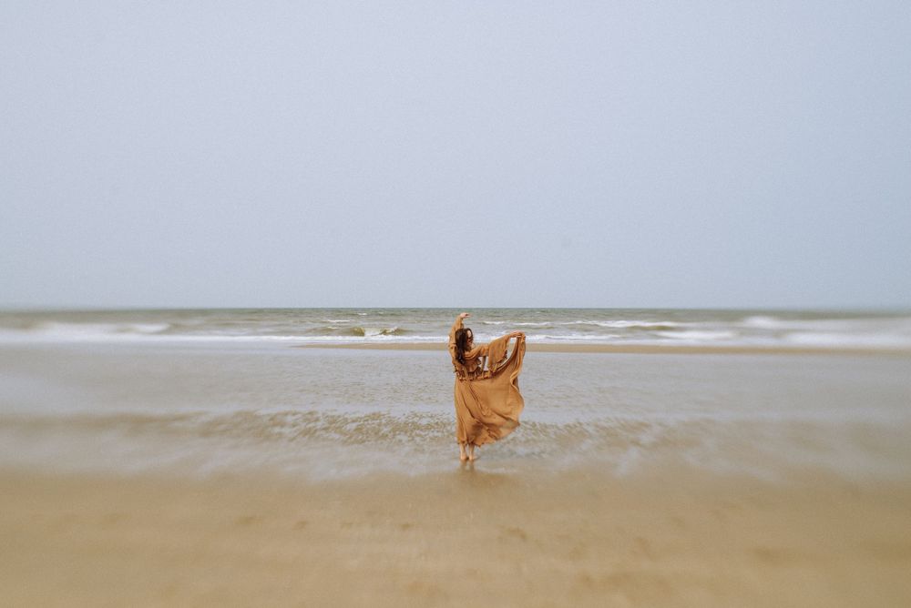 A figure walks along a misty beach shoreline with waves rolling in.