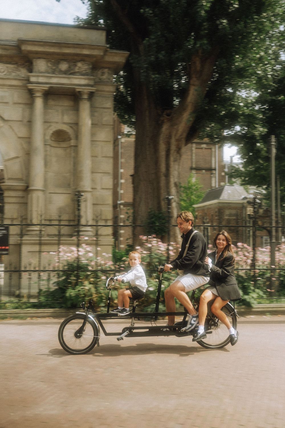 People riding recumbent bikes along a path near classical stone architecture.