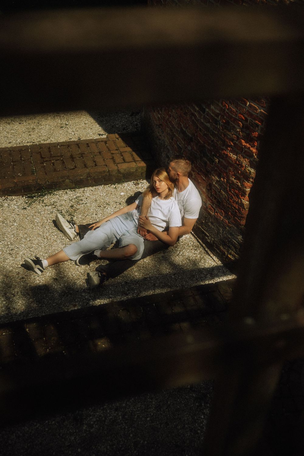 A couple rests in shadow against a brick wall on a sunny afternoon.