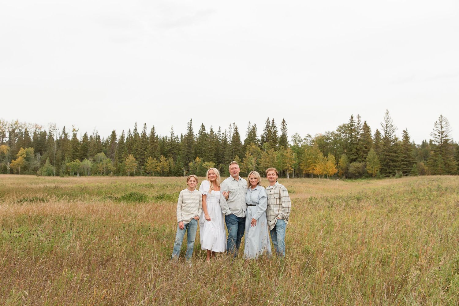 A small group stands together in a grassy field with evergreen trees in the background.