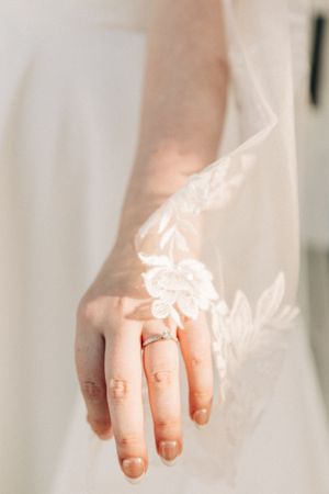 A delicate close-up of hands holding a sheer white bridal veil in soft natural light.