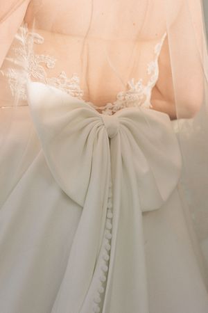 Elegant white bridal gown with a large decorative bow detail on the back creating a romantic silhouette.