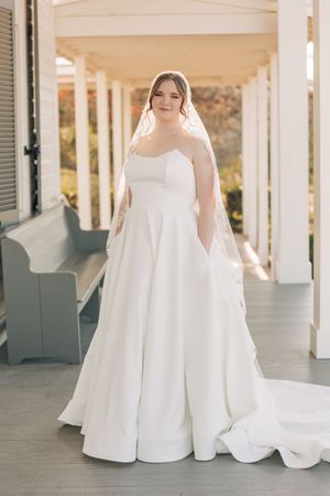 Classic white strapless ballgown wedding dress with pockets and cathedral veil on a covered porch setting.
