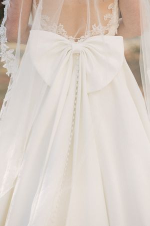 Close up of an elegant white wedding dress back detail featuring a large decorative bow and delicate lace overlay.