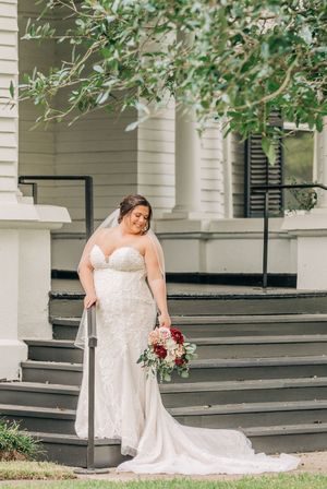 A bride in a flowing white lace dress poses gracefully on the steps of a white columned building.