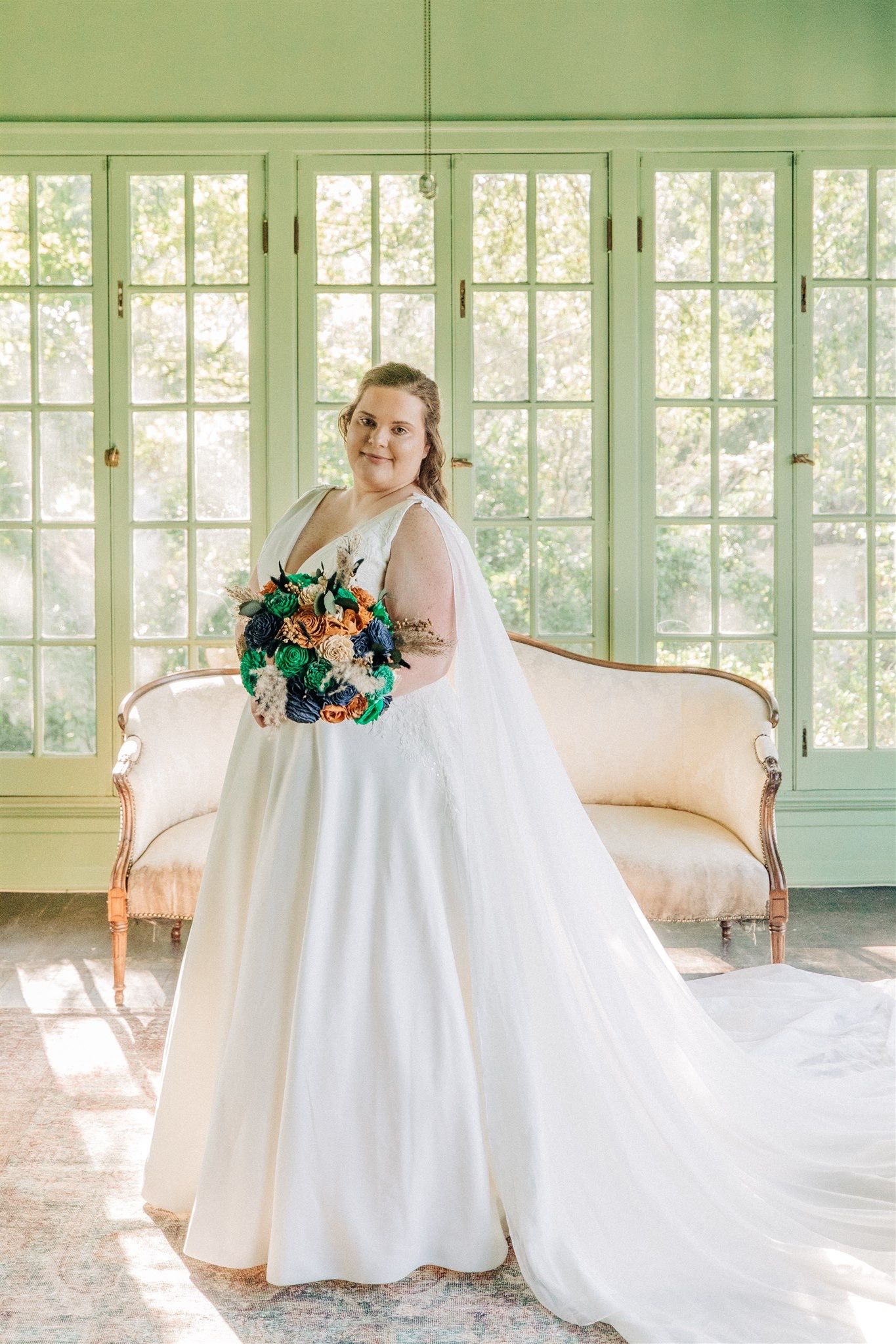 A wedding photo in a bright sunlit room with french windows and a vintage cream-colored sofa.