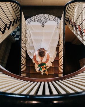 Aerial view of wedding dress and person walking on spiral staircase with black and white striped railings creating geometric pattern.