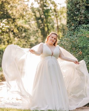 Bride in elegant white plus size wedding gown twirls gracefully in a sunlit garden setting.