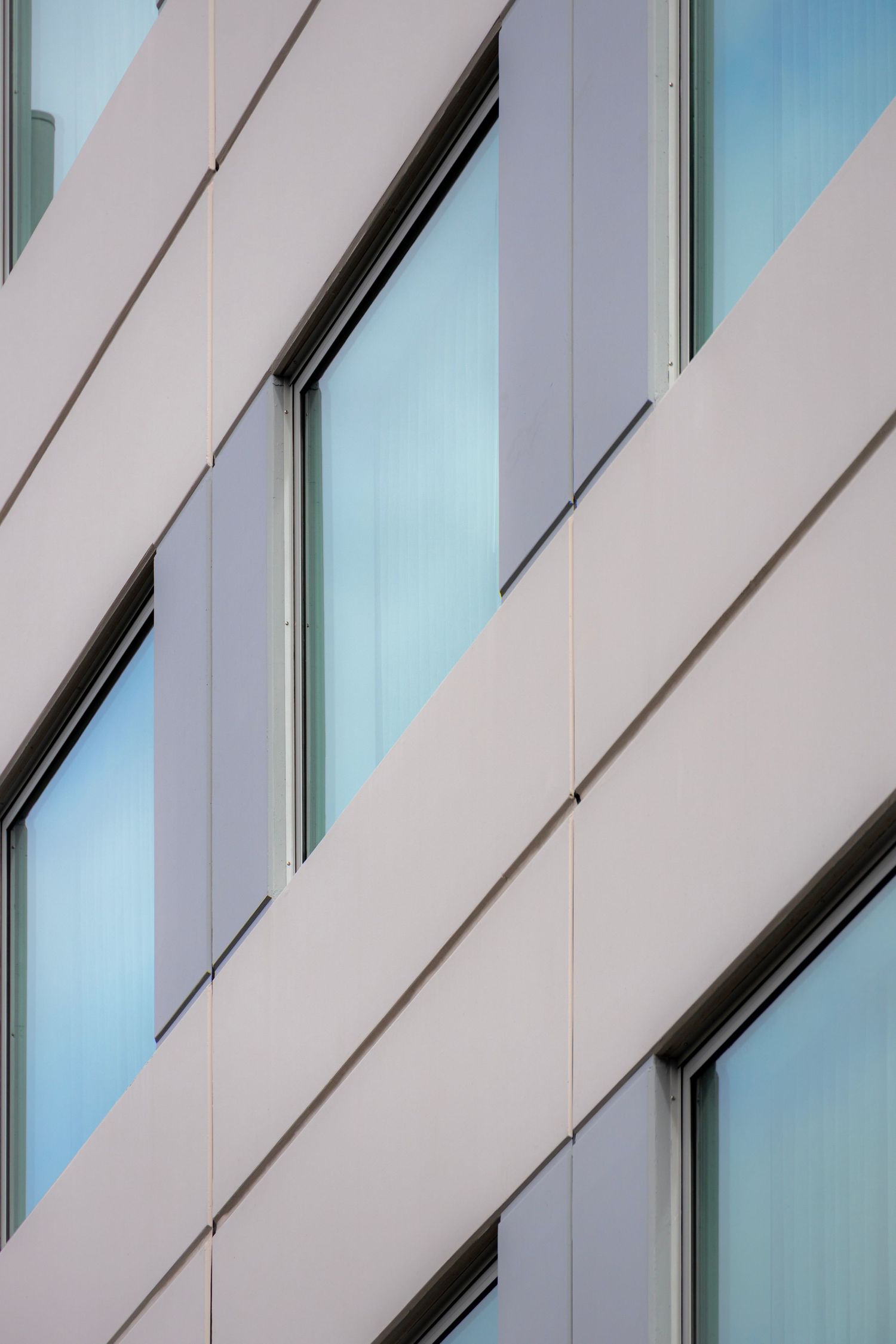 Beige and grey diagonal facade lines intersect with frosted windows in a soft, structured rhythm.