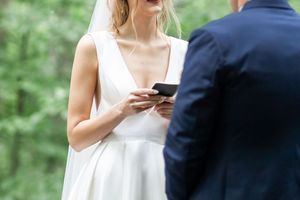 Someone in a white wedding dress checks their phone while standing with someone in a navy suit outdoors.