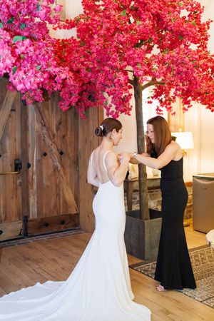 A wedding gown fitting with an elegant backless white dress and stunning pink floral decor overhead in a rustic venue.