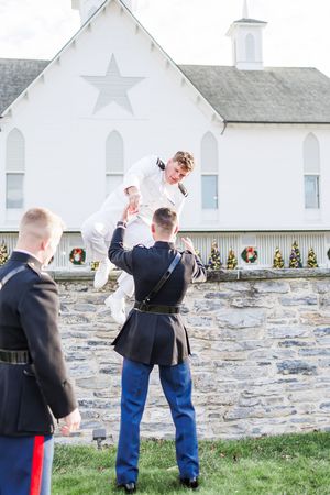 A military ceremony takes place outside a white church with a stone wall and star decoration.