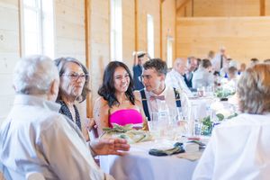 Guests enjoy conversation and dining at an elegant reception with white tablecloths and natural lighting through windows.