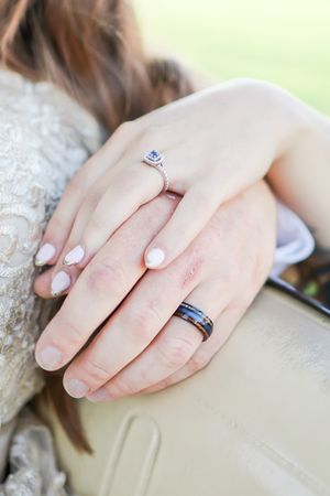 Close-up photo of hands showing engagement ring and matching wedding band with white manicured nails.