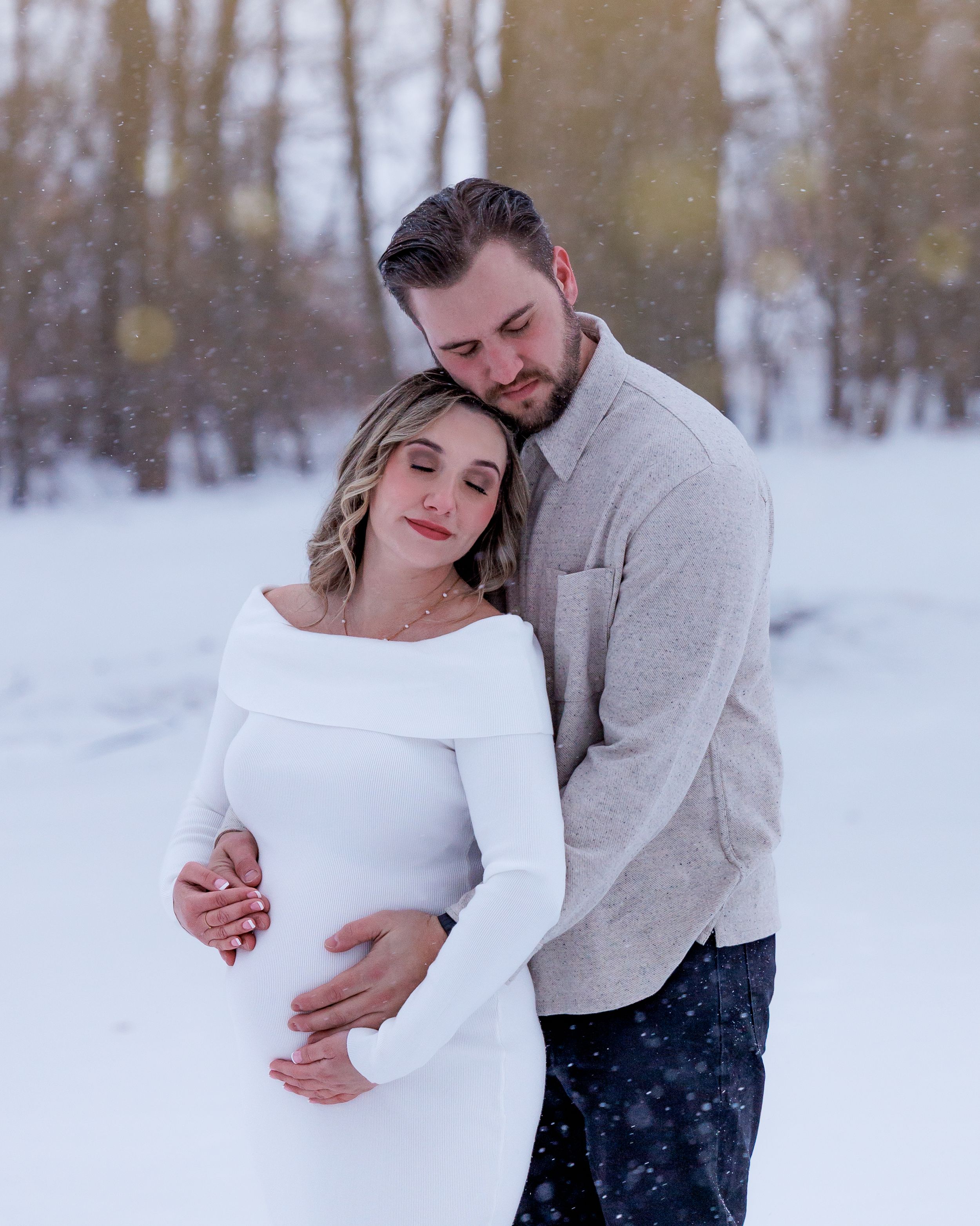 A couple shares an intimate winter moment in the snow wearing white and gray outfits.