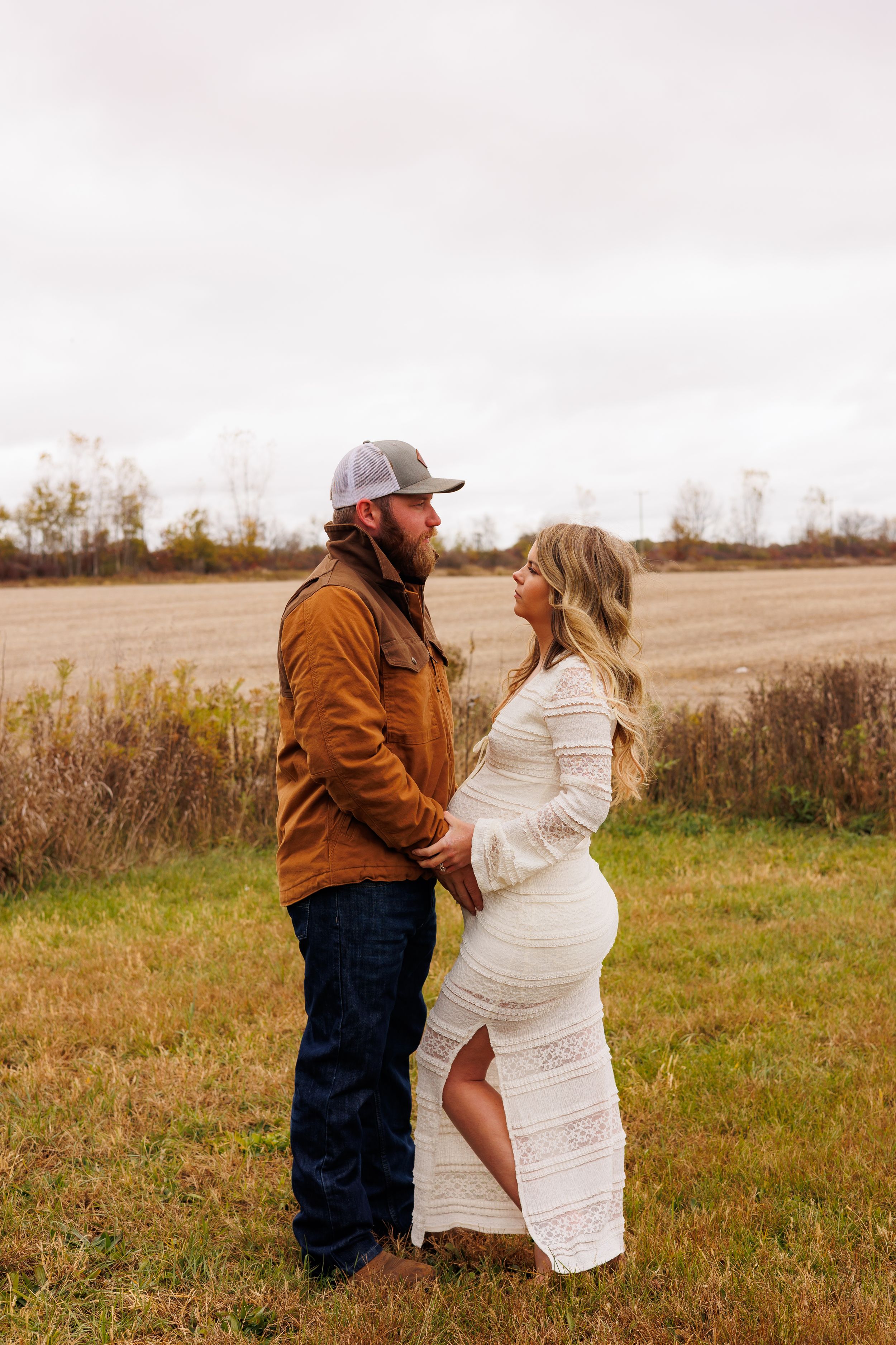 A couple in a field shares a tender moment as they embrace against an autumn backdrop.