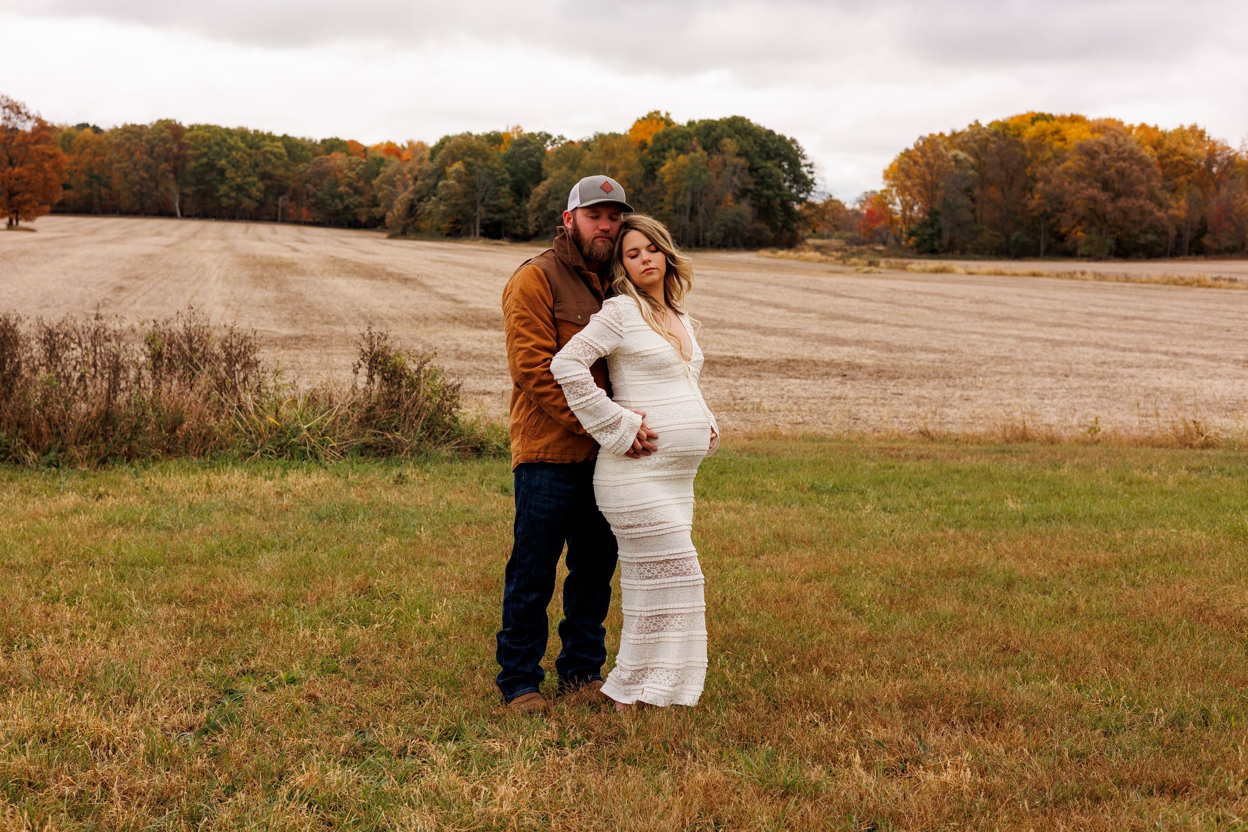 Romantic couple embraces in a golden autumn field during sunset while wearing rustic wedding attire.