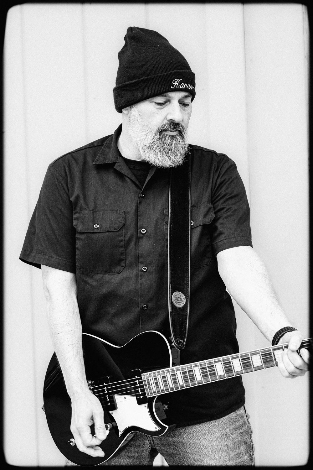 Black and white photo series of musician playing electric bass guitar while wearing dark clothes and beanie.