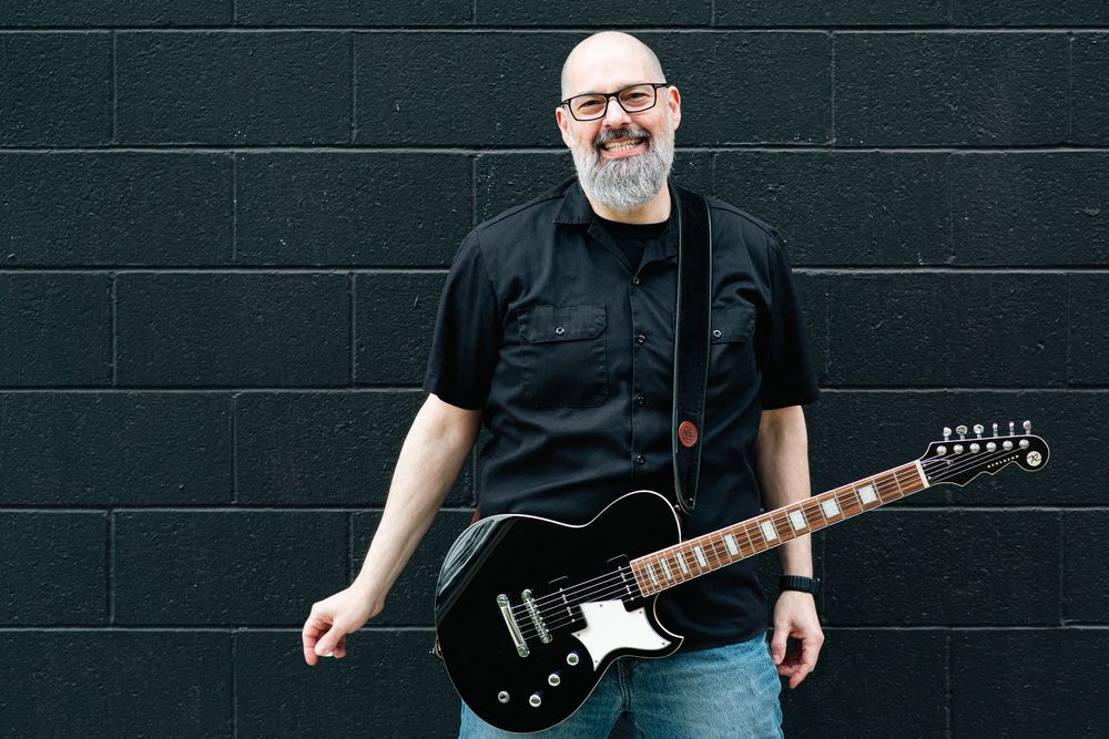 Black electric guitar being played against dark background in multiple poses during performance.