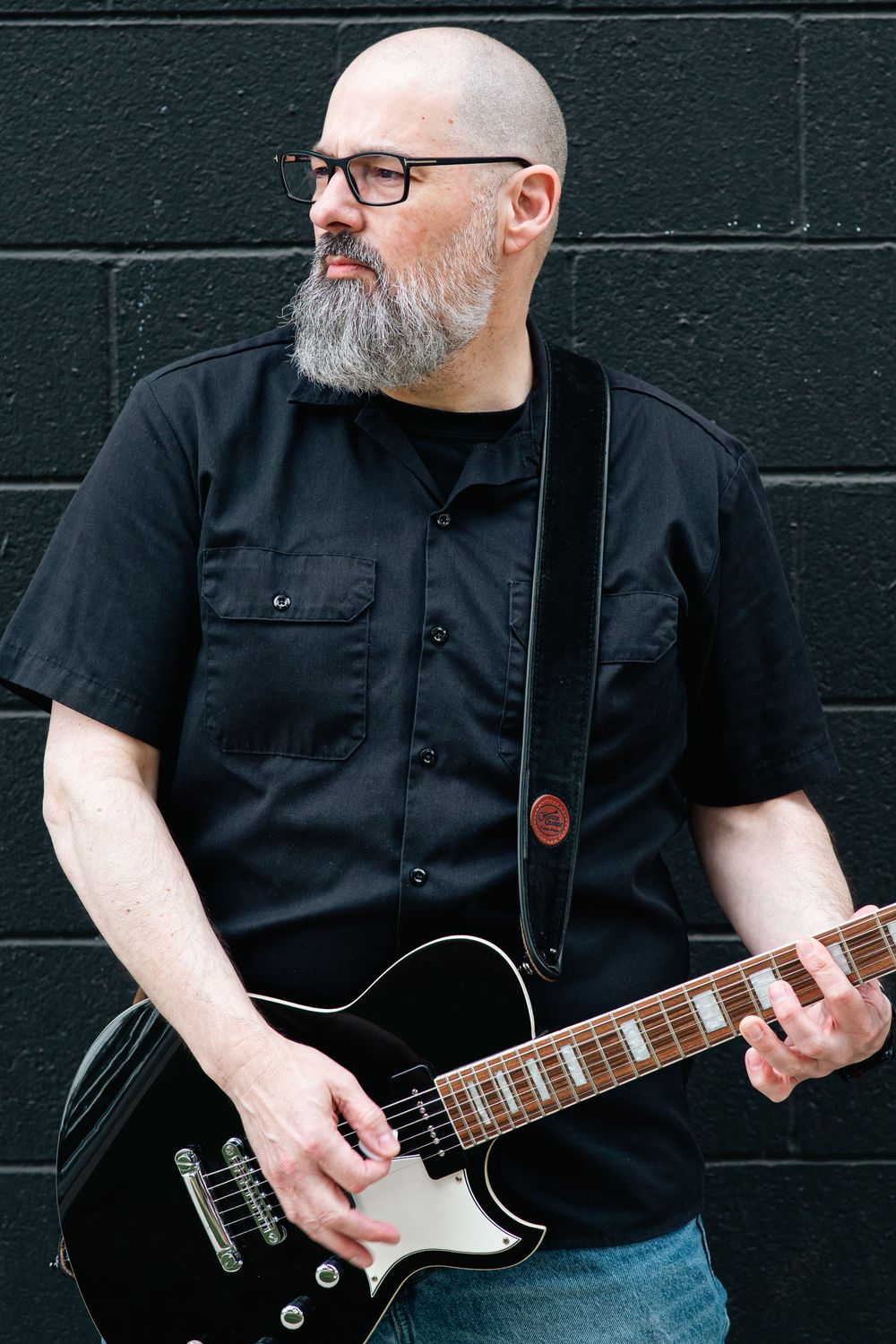Musician in black shirt playing electric guitar against dark wall in sequence of progressive action shots.