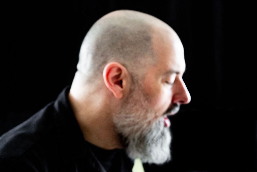 Side profile silhouette of a bald man with a white beard against black background.