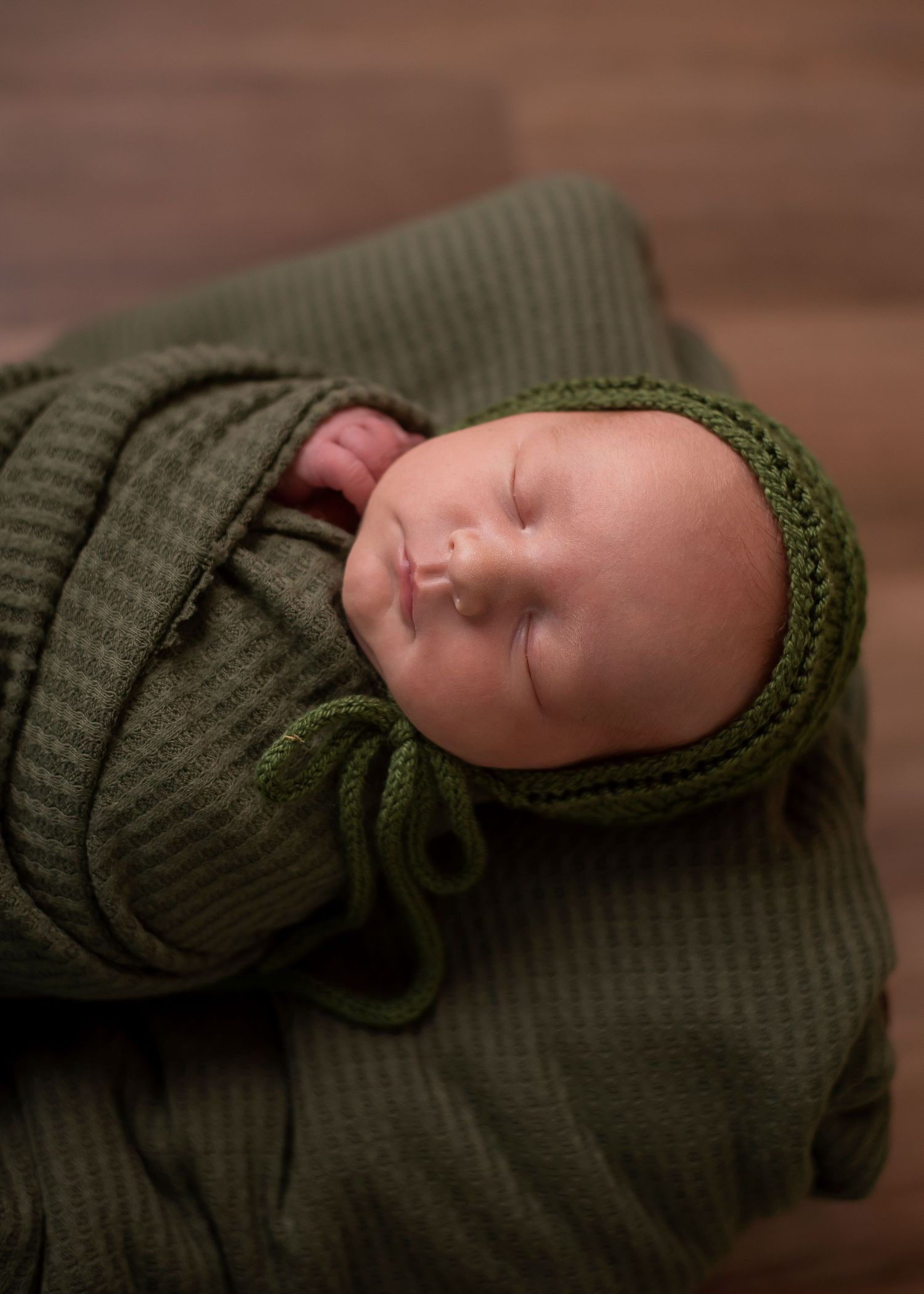 Sleeping newborn baby is swaddled in a cozy olive green knit blanket.