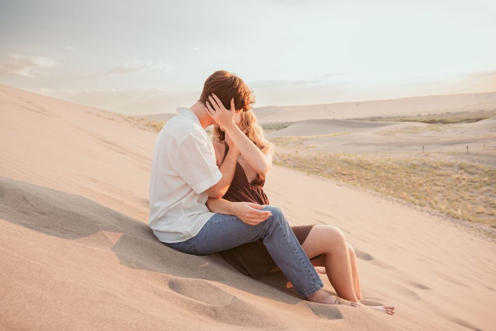 Couple sitting together on sand dunes at sunset in a desert landscape.