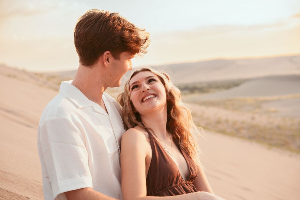 A happy couple shares a loving moment together while standing in a desert landscape at sunset.