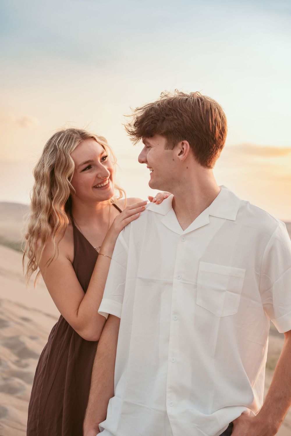 Playful couple laughing together against sunset background on sandy dunes.