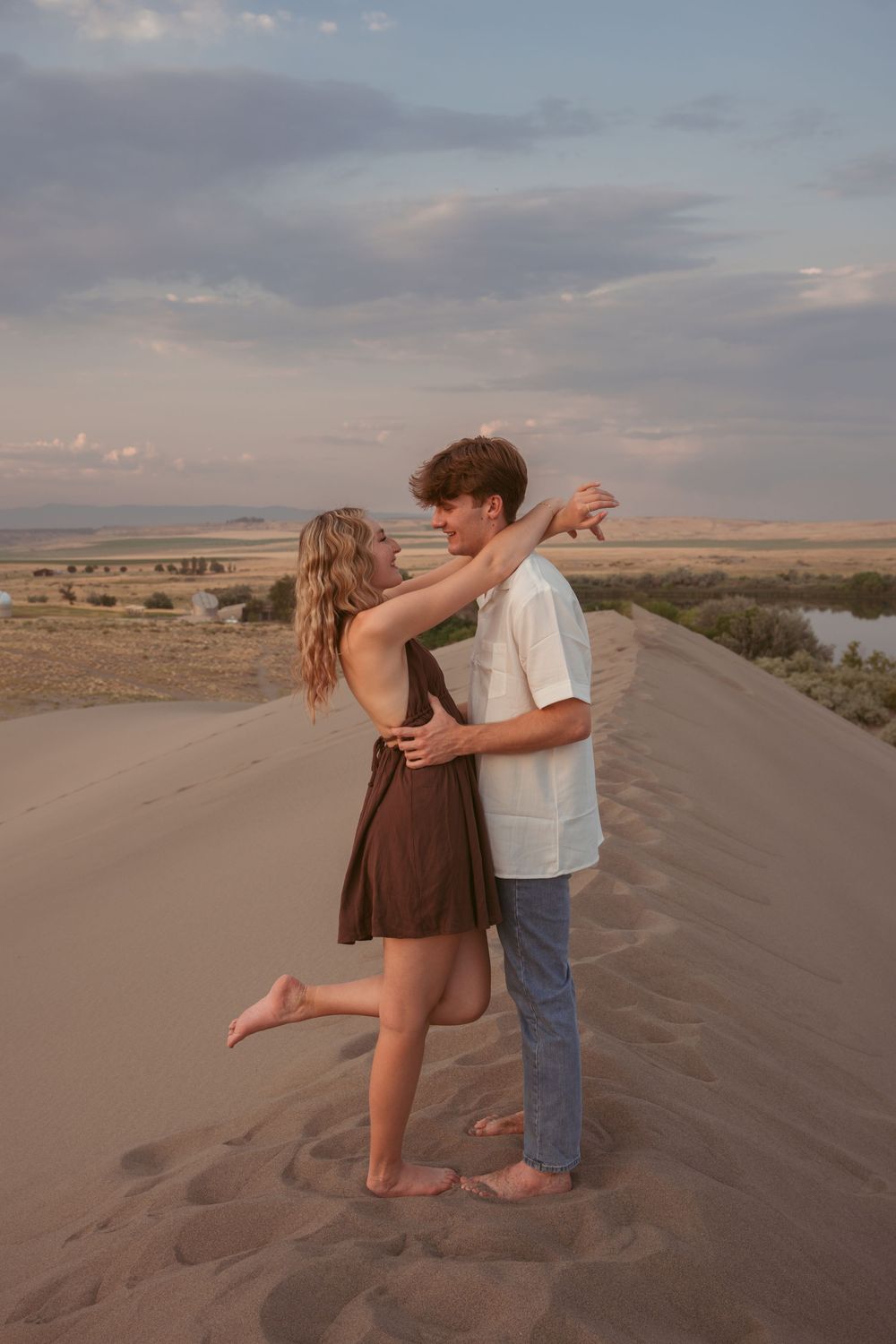 Romantic couple embracing on sandy dunes during golden hour with desert landscape in background.
