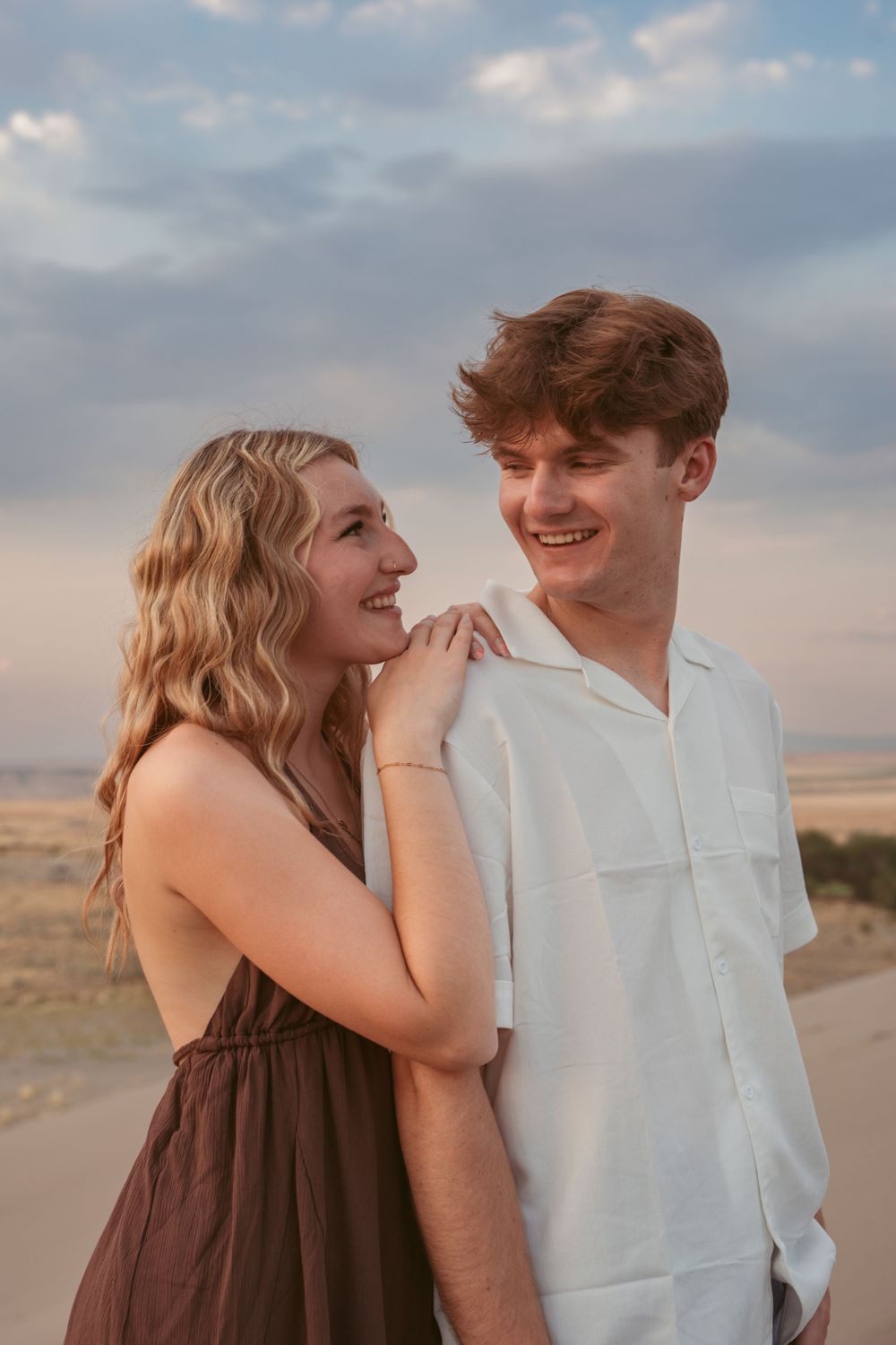 A couple shares a joyful moment together against a desert landscape at sunset.