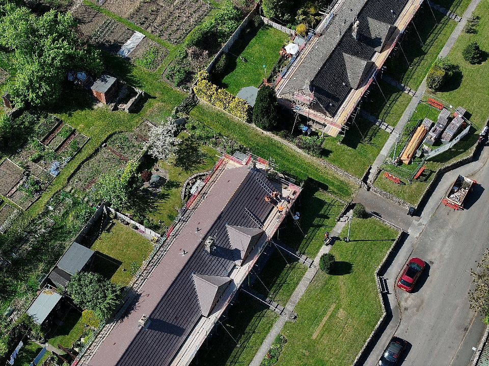 Aerial view of church buildings and cemetery grounds with parked cars along road and green landscaping.