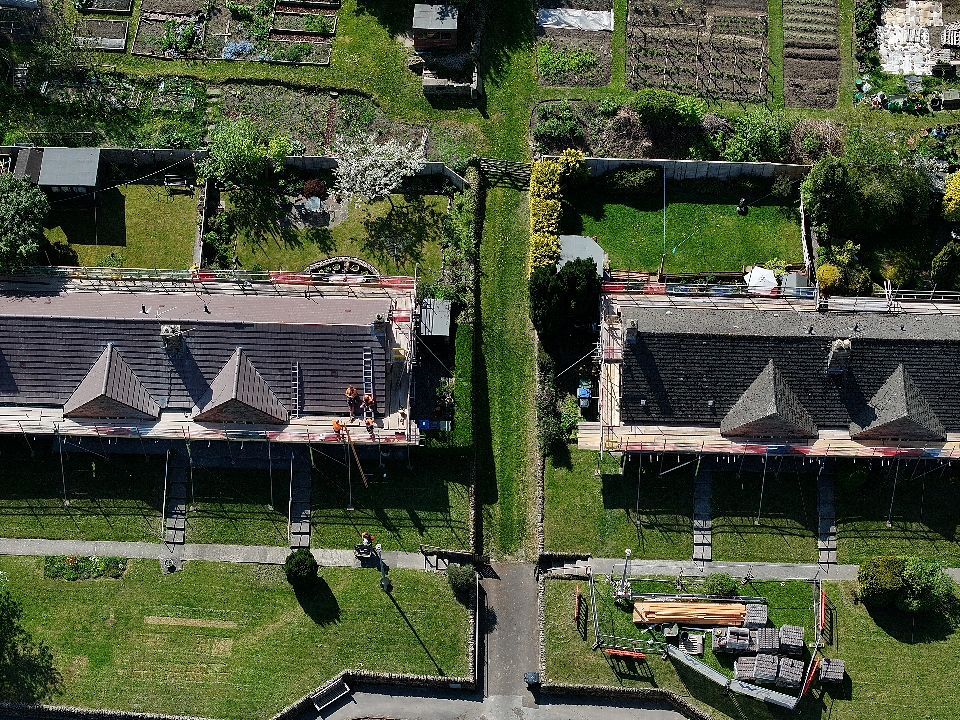 Aerial view of row houses with gray roofs and long narrow residential gardens in a suburban neighborhood.