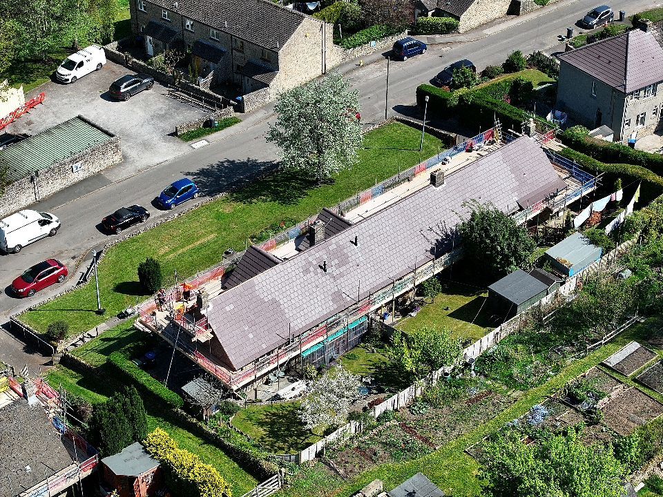 Aerial view of a residential property with garden plots, outbuildings and multiple parked vehicles in a suburban area.