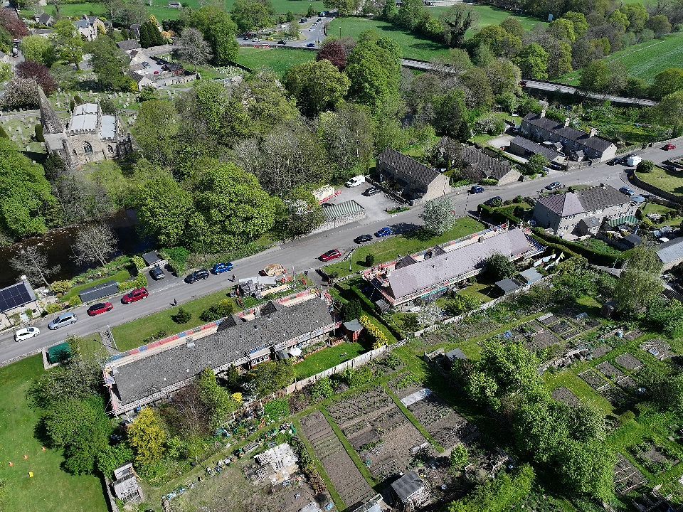 Aerial view of a residential area with allotments and gardens surrounded by lush green trees and houses.